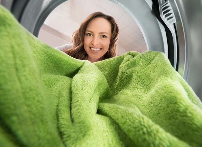 Smiling woman viewed from inside washing machine holding green towel.