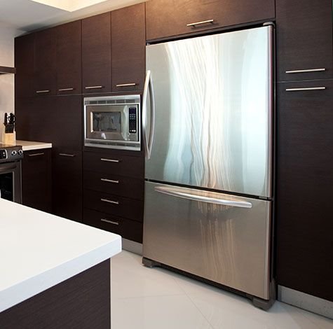 Stainless steel refrigerator built into dark wood kitchen cabinetry.
