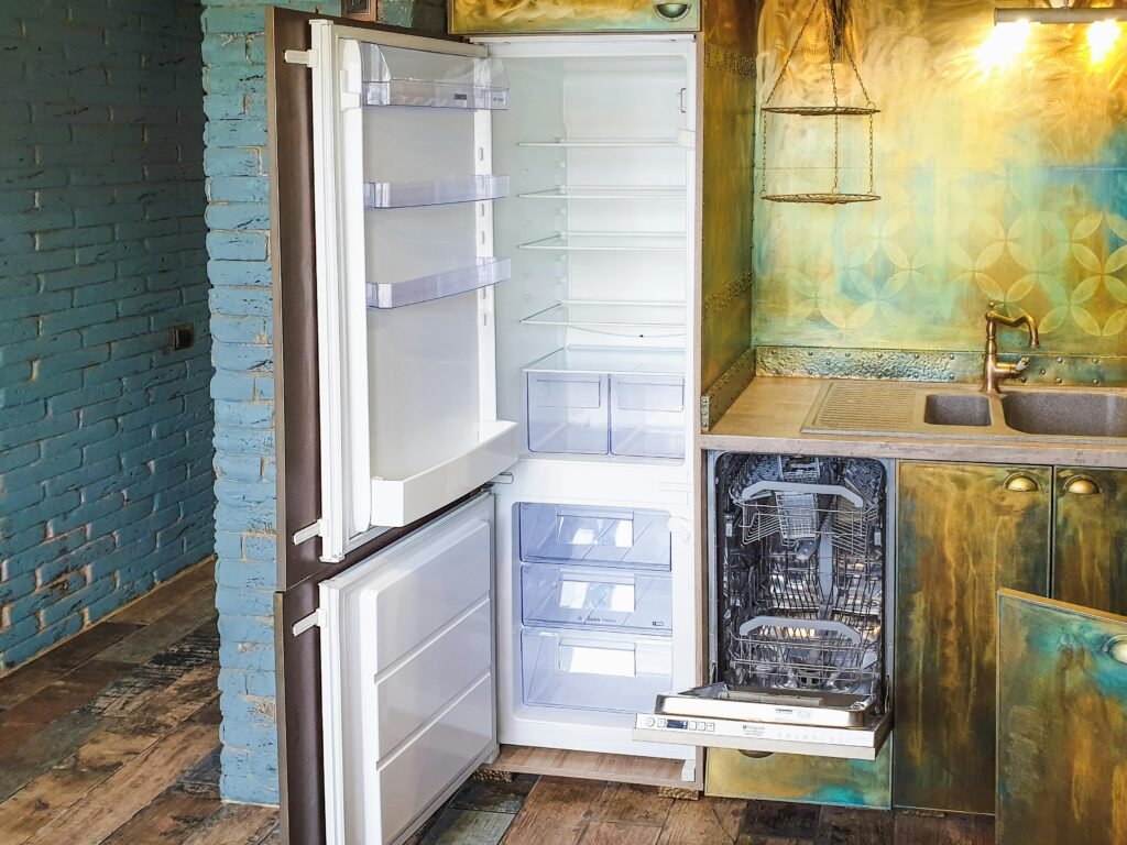 Empty open refrigerator beside open dishwasher in rustic patterned kitchen.