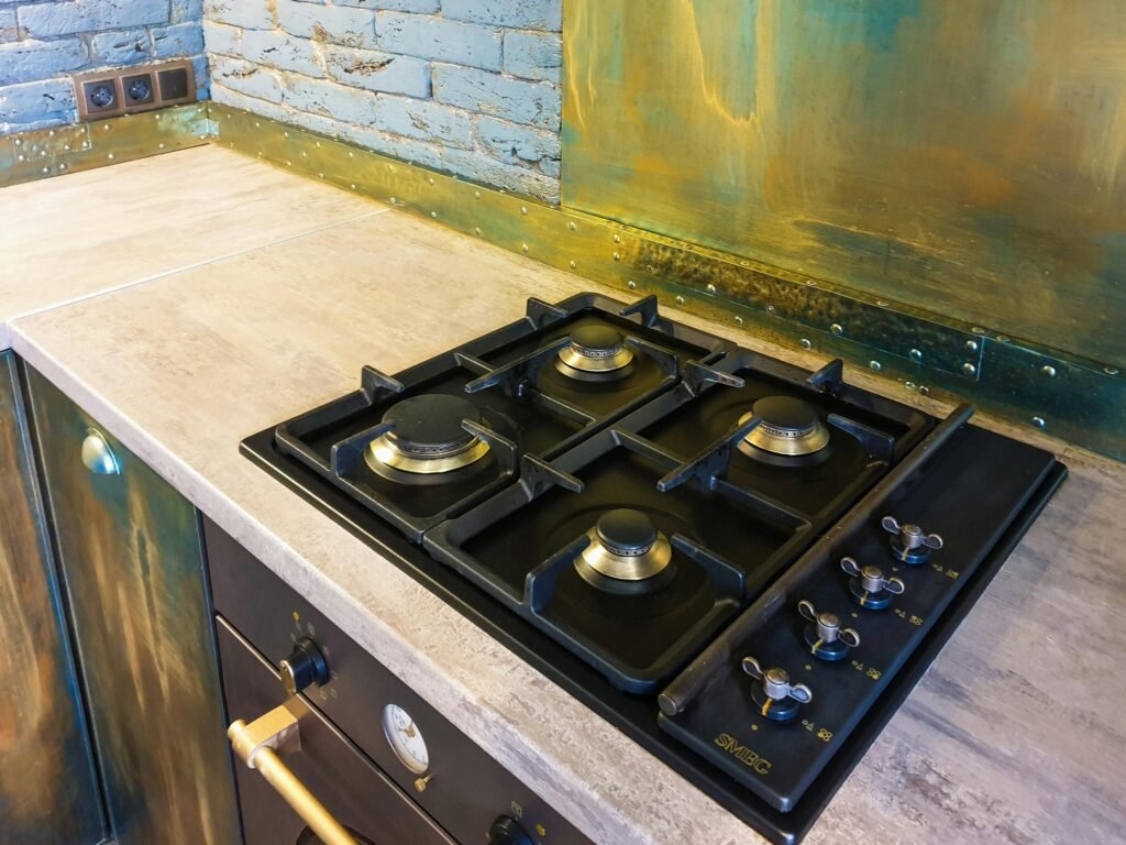 Black gas cooktop with brass knobs set into stone countertop.