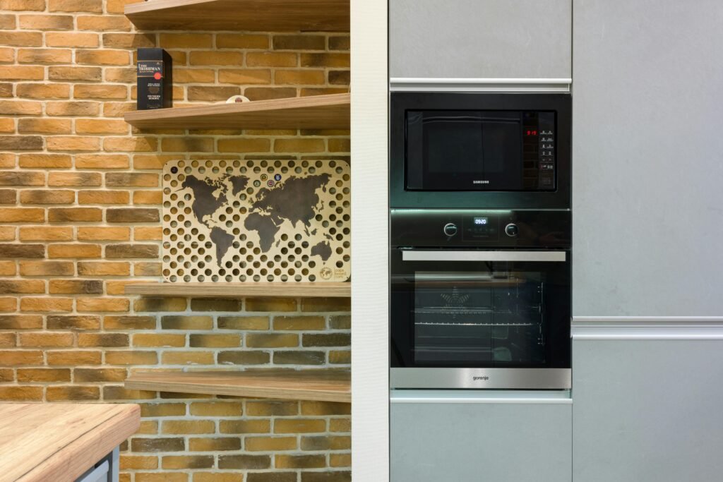 Modern kitchen with exposed brick shelving on one side and built-in black microwave and oven set into gray cabinetry on the other