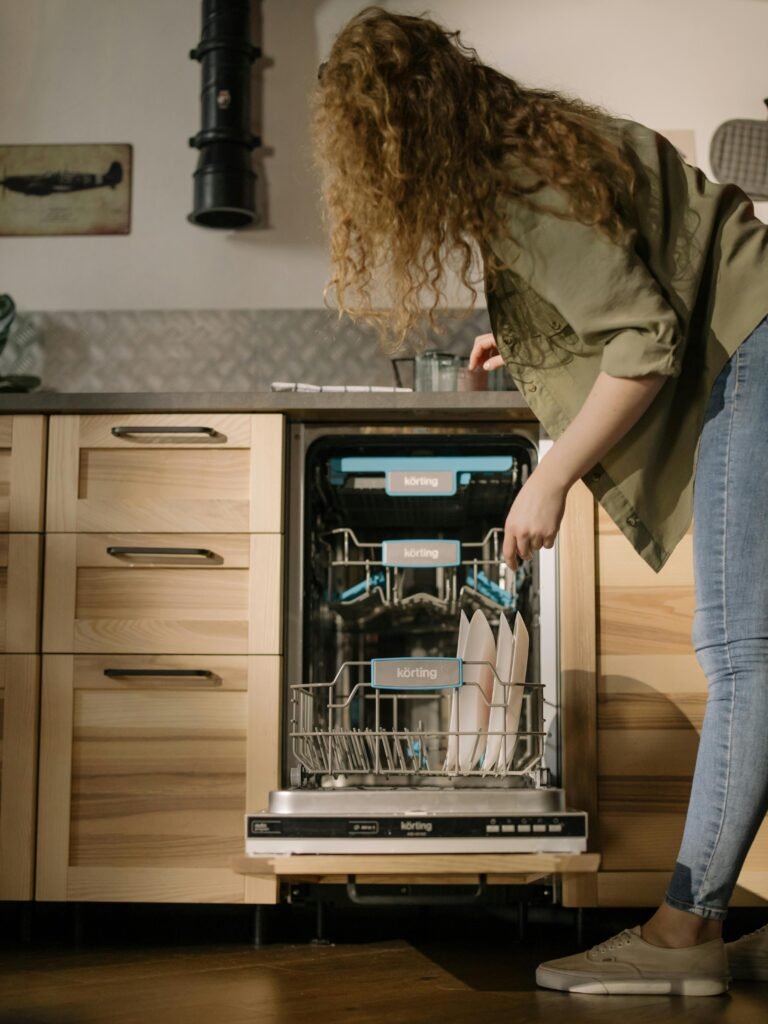 Woman with curly hair loading dishes into open dishwasher.