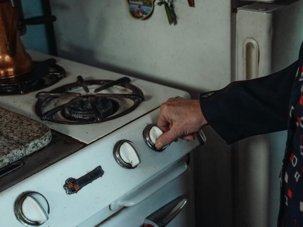 Hand turning knob on old white gas stove with cast iron burners.