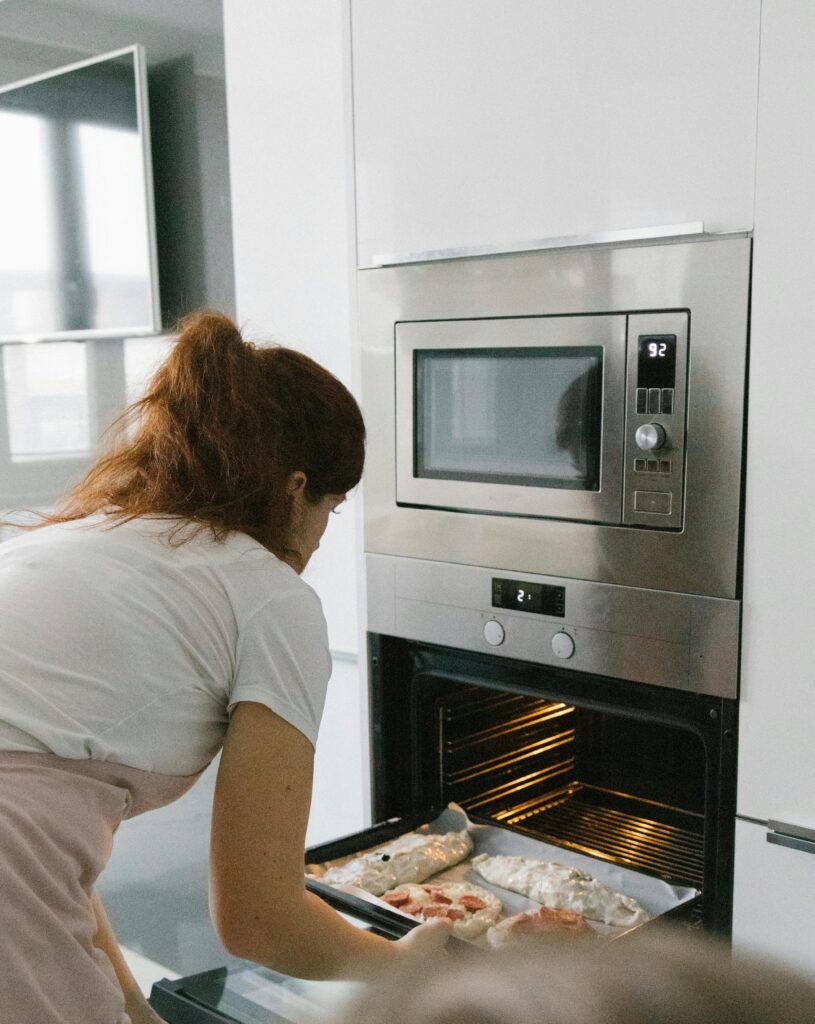 Woman placing pizza tray into open built-in oven under microwave.