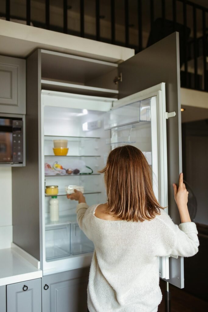 Woman looking inside open refrigerator, reaching for food container.