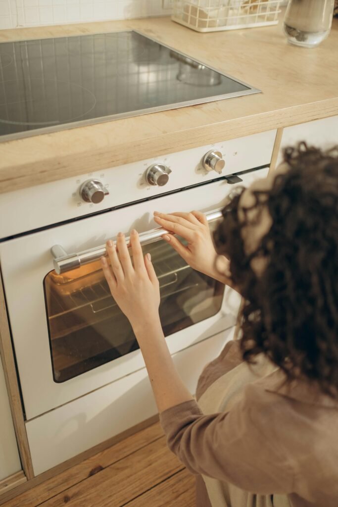 Woman with curly hair checking food inside a white built-in oven.
