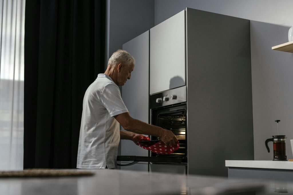 Older man using oven mitts to remove dish from built-in oven.