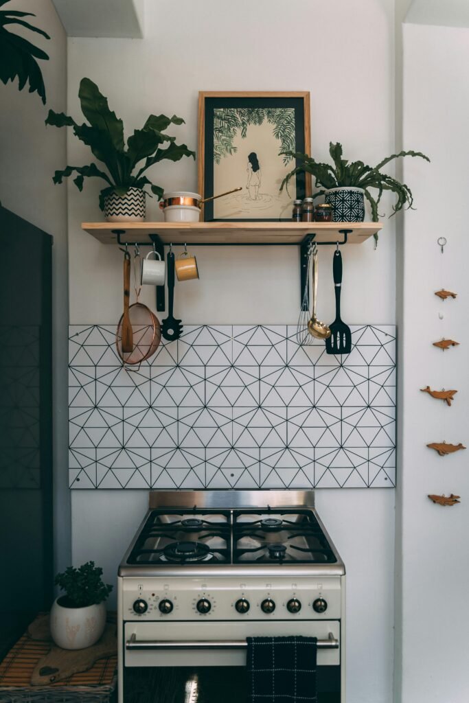 Vintage cream gas stove below geometric tile wall with hanging kitchen tools.